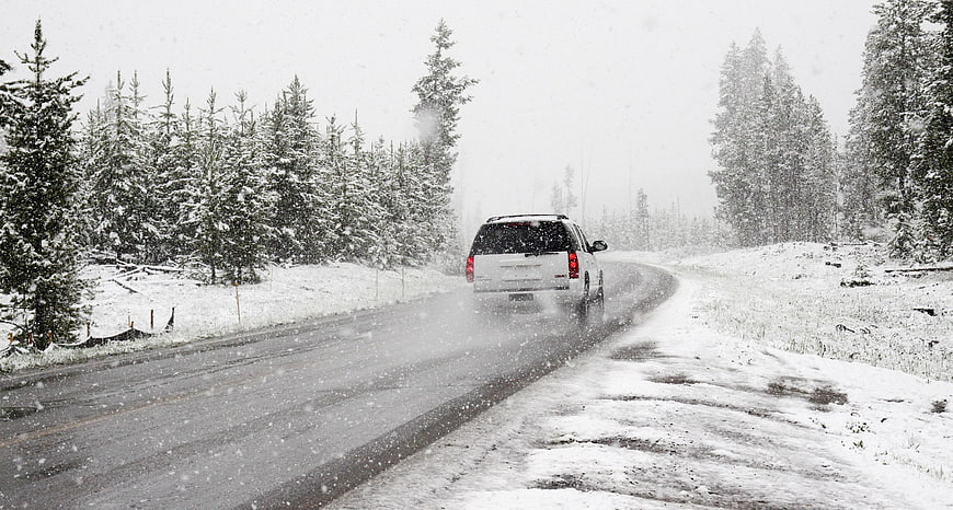 White SUV Driving on Snowy Road in Winter Forest