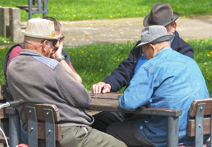 Senior Men Playing Dominoes At Park Table