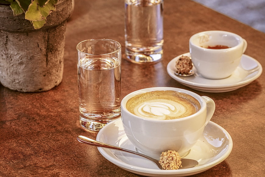 Cappuccino with Latte Art and Water Glasses on Rustic Wooden Table