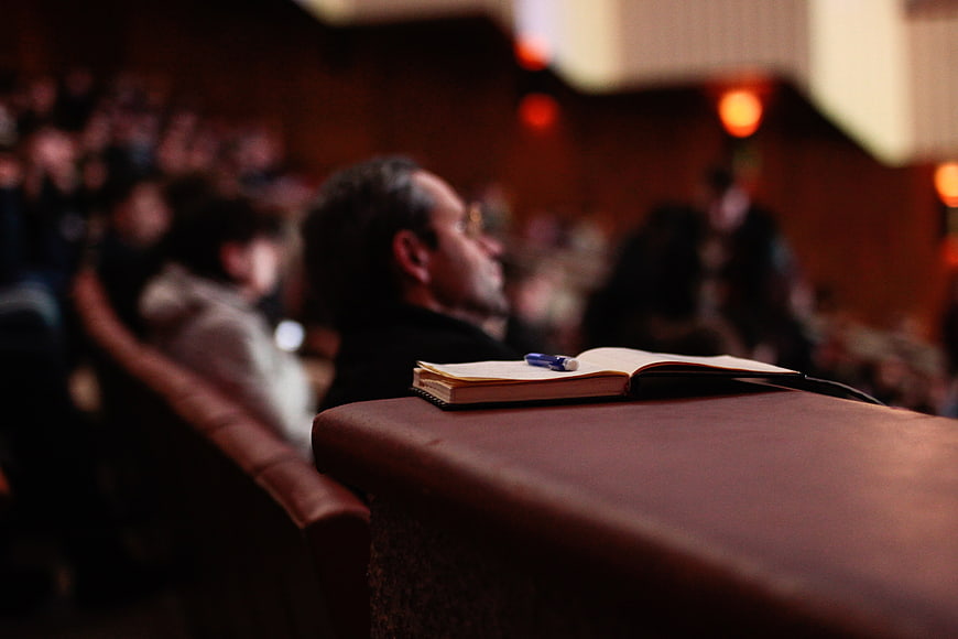 Open notebook and pen in blurred auditorium audience