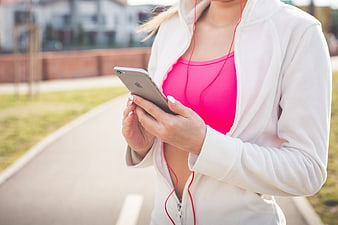 Woman in white jacket and pink top using smartphone with red earphones outdoors