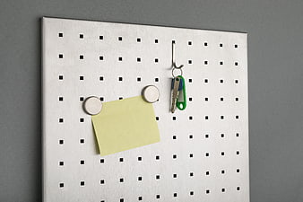 White pegboard with yellow sticky note and keys hanging on hook