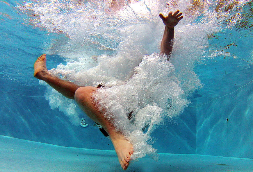 Underwater shot of person diving into swimming pool with bubbles
