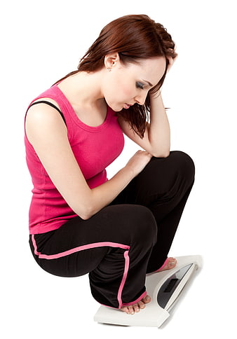Sad woman squatting on bathroom scale looking worried