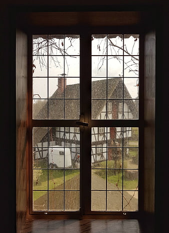 Rainy View Through Wooden Window to Half-Timbered House