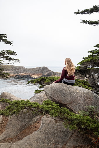 Woman sitting on coastal rocks overlooking ocean view