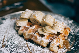 Close-up of waffle with sliced bananas and powdered sugar