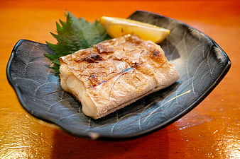 Grilled Fish Fillet on Black Ceramic Plate with Lemon and Shiso
