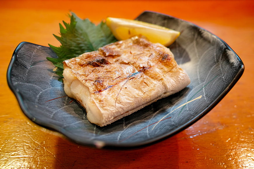 Grilled Fish Fillet on Black Ceramic Plate with Lemon and Shiso