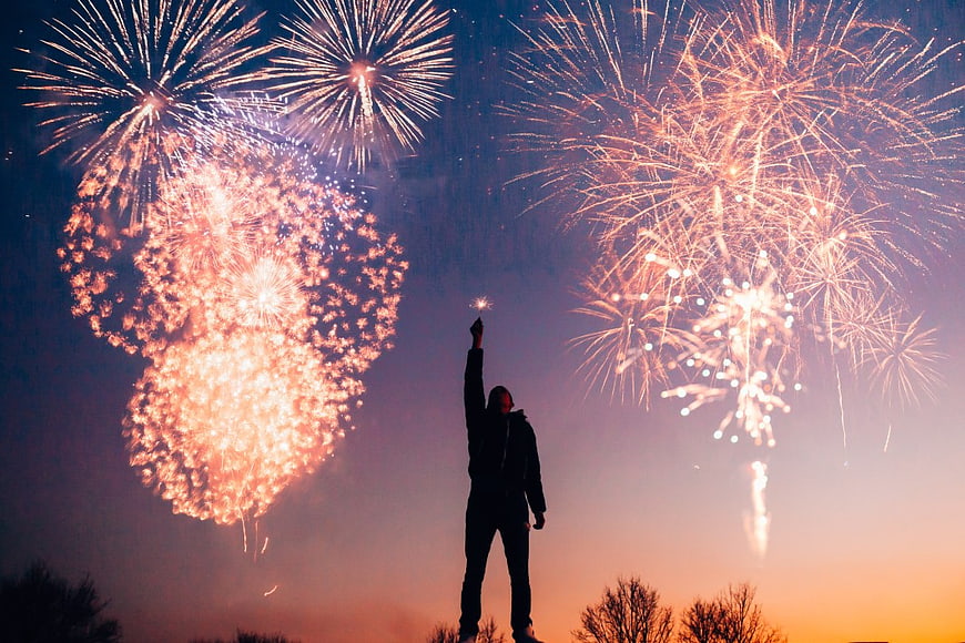 Silhouette of Man Holding Sparkler Under Fireworks