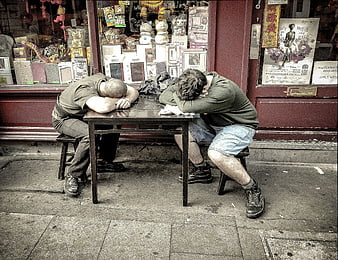 Two Men Sleeping at Outdoor Table in Front of Shop