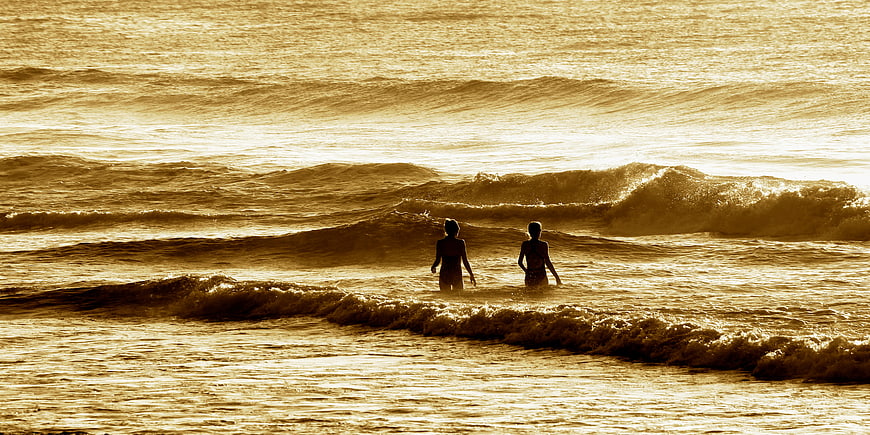 Silhouettes of Two Women Swimming in Golden Ocean Waves