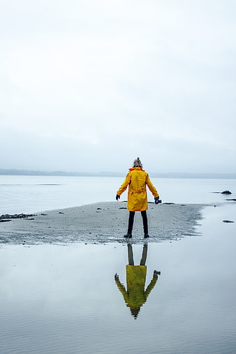 Woman in Yellow Raincoat Standing on Beach with Reflection