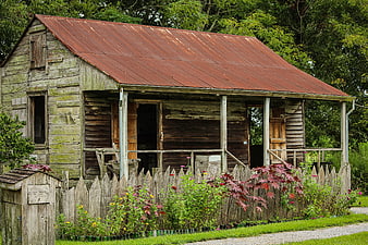 Weathered wooden slave cabin with red roof and picket fence