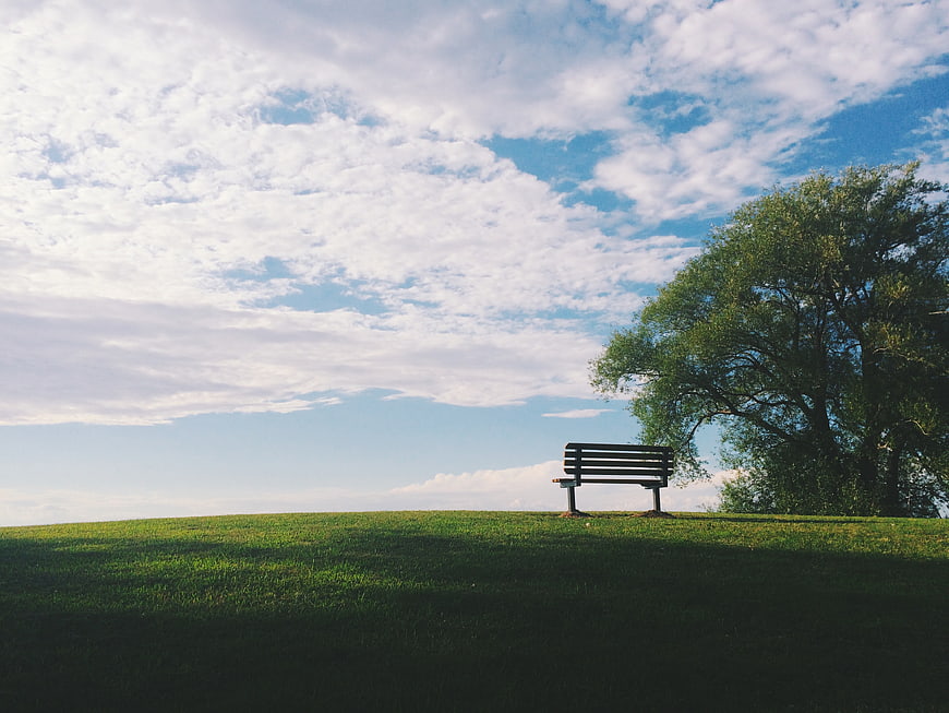 Lone Park Bench on Grassy Hill Under Cloudy Sky