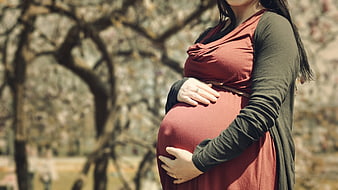 Pregnant woman holding belly outdoors in spring