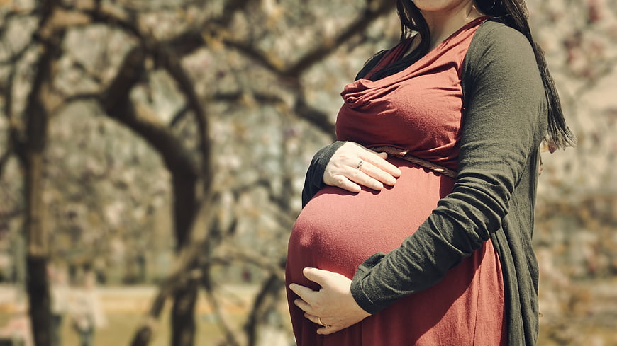 Pregnant woman holding belly outdoors in spring