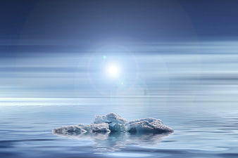 Small iceberg floating in calm blue water with bright sun flare
