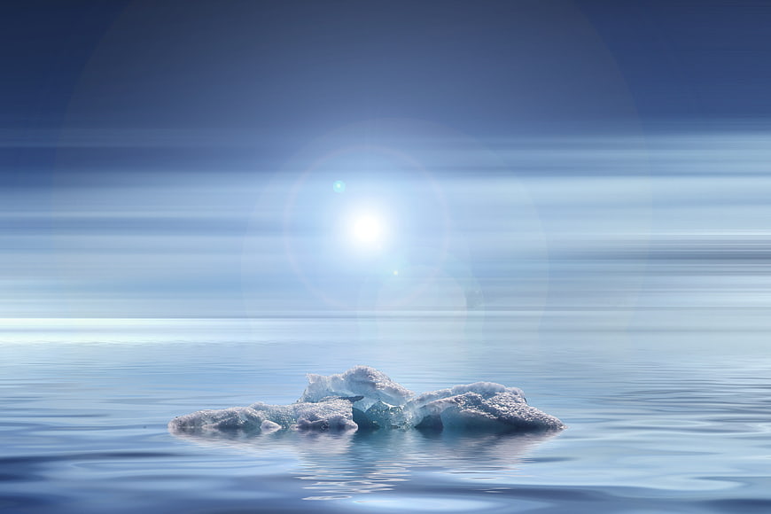 Small iceberg floating in calm blue water with bright sun flare