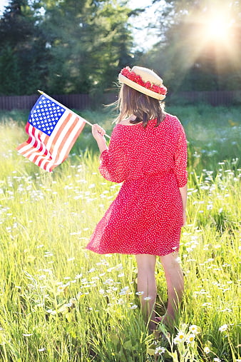 Woman in red dress holding American flag in wildflower meadow
