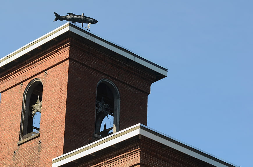 Brick mill tower with fish weathervane against blue sky
