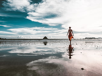 Woman in Orange Dress Walking on Wet Beach with Sky Reflection
