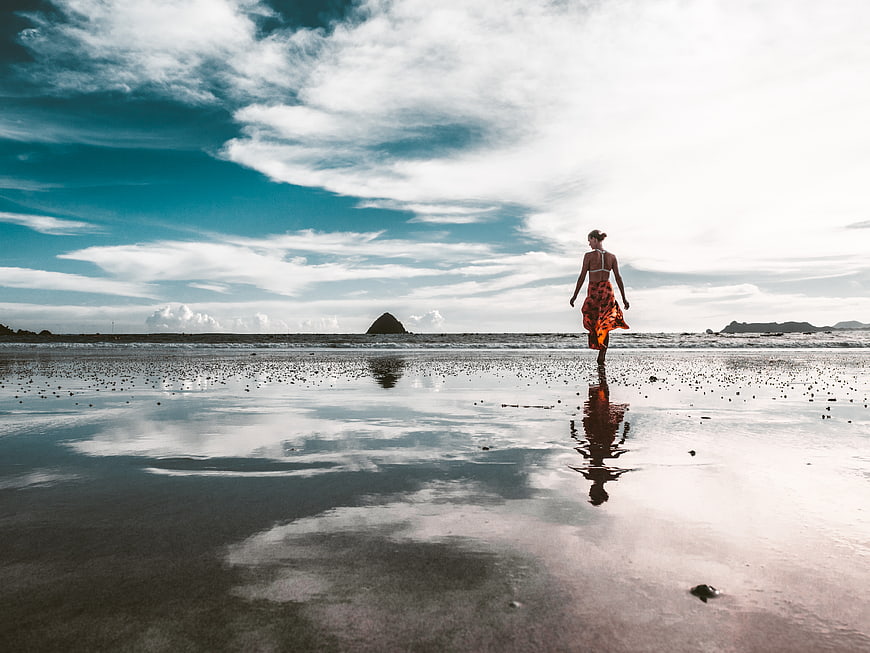 Woman in Orange Dress Walking on Wet Beach with Sky Reflection