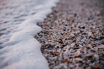Close-up of sea foam washing over a pebble and shell beach