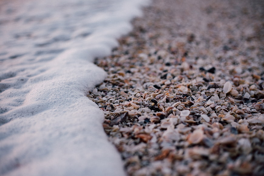 Close-up of sea foam washing over a pebble and shell beach