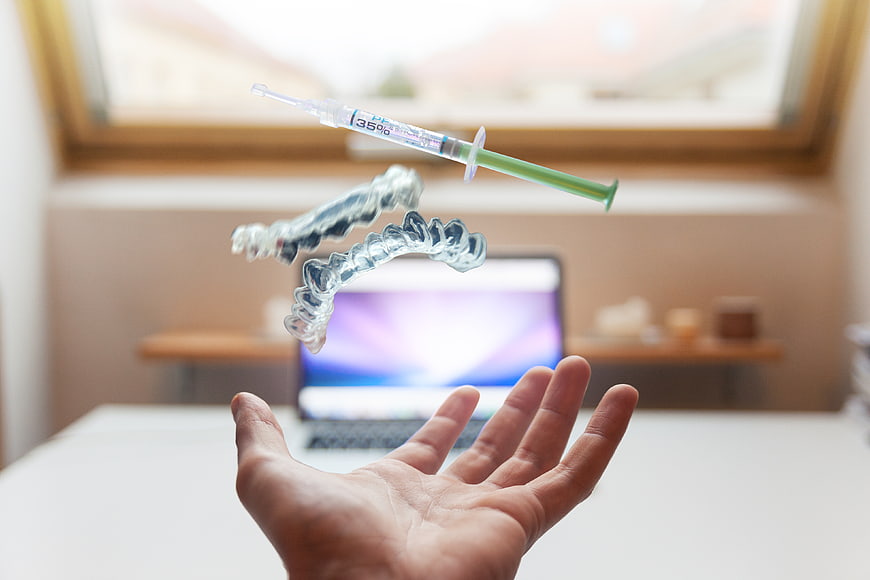 Dental aligners and syringe floating above hand