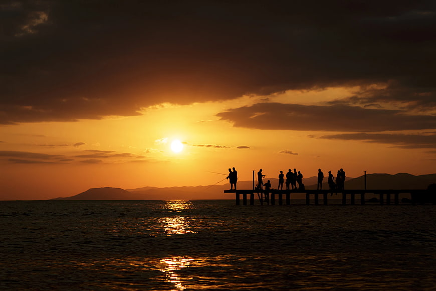 Silhouettes of People Fishing on a Pier at Sunset