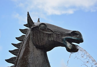Bronze horse head statue fountain spouting water against blue sky