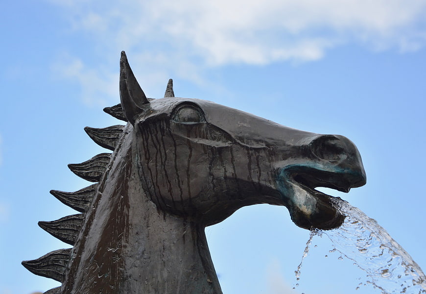 Bronze horse head statue fountain spouting water against blue sky