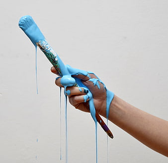 Hand holding paintbrush with dripping blue paint against white background