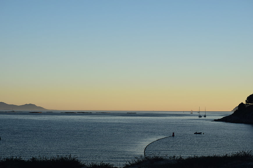 Serene coastal sunset with sailboats and distant mountains