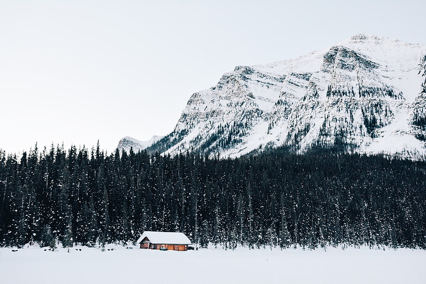 Solitary wooden cabin in snowy mountain landscape with pine forest