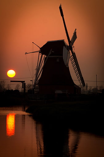 Silhouette of traditional windmill at sunset over canal