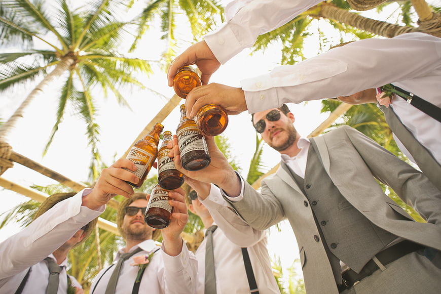 Groomsmen in Suits Toasting with Beer Bottles Under Palm Trees