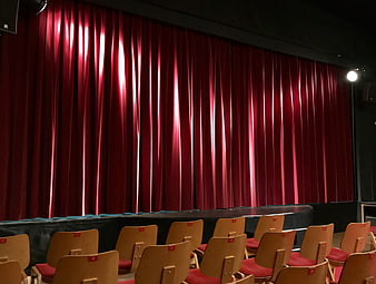 Empty theater stage with red velvet curtain and wooden seating