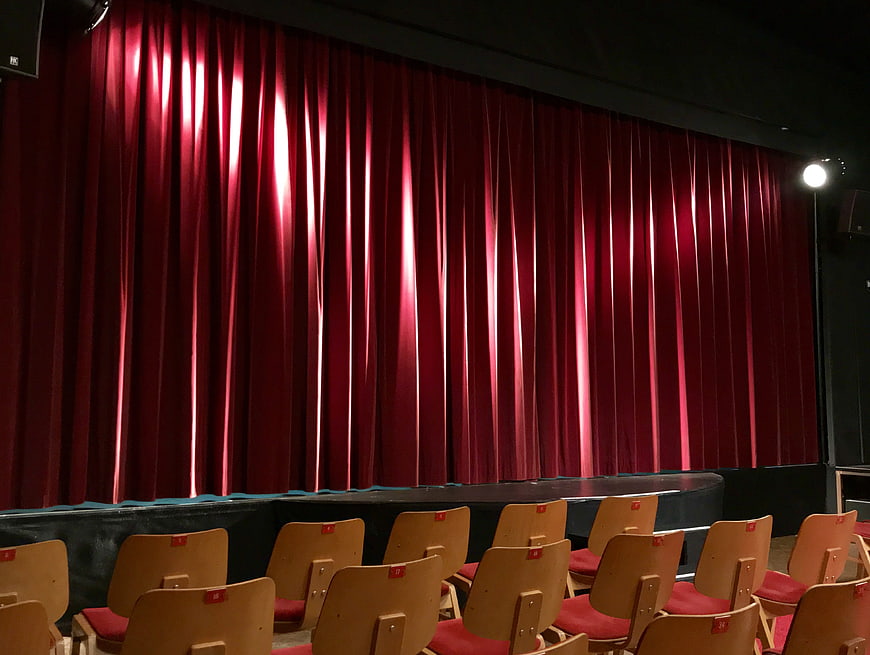 Empty theater stage with red velvet curtain and wooden seating