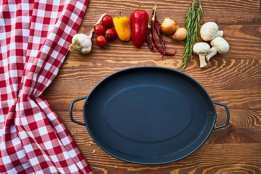Empty black baking pan with fresh vegetables on wooden table
