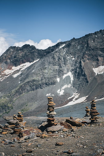 Stacked stone cairns on rocky mountain ridge with snow-capped peaks