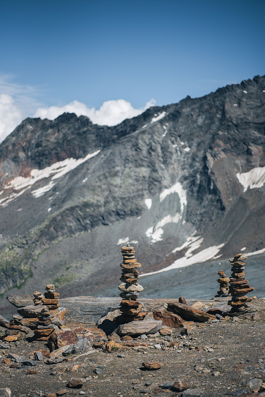 Stacked stone cairns on rocky mountain ridge with snow-capped peaks