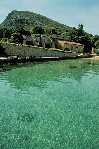 Crystal clear turquoise water with stone buildings and green hill