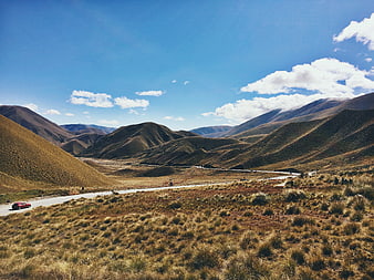 Red car driving on winding mountain road through grassy hills