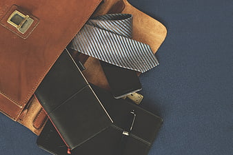 Flat lay of brown leather briefcase with tie and notebook