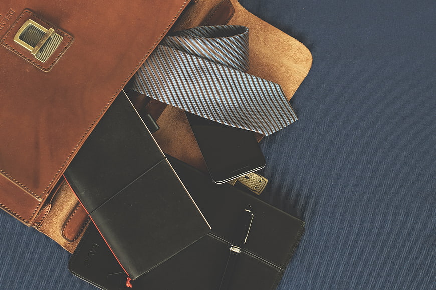 Flat lay of brown leather briefcase with tie and notebook