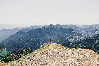 Hiker standing on rocky mountain ridge overlooking vast forested valley