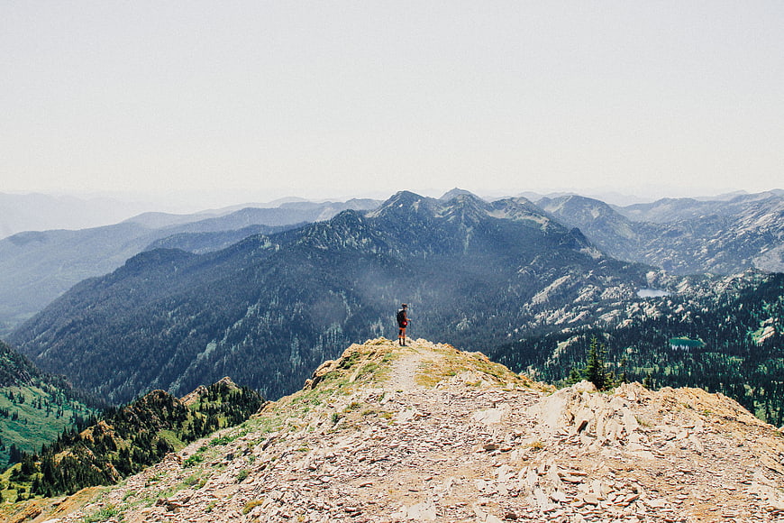 Hiker standing on rocky mountain ridge overlooking vast forested valley