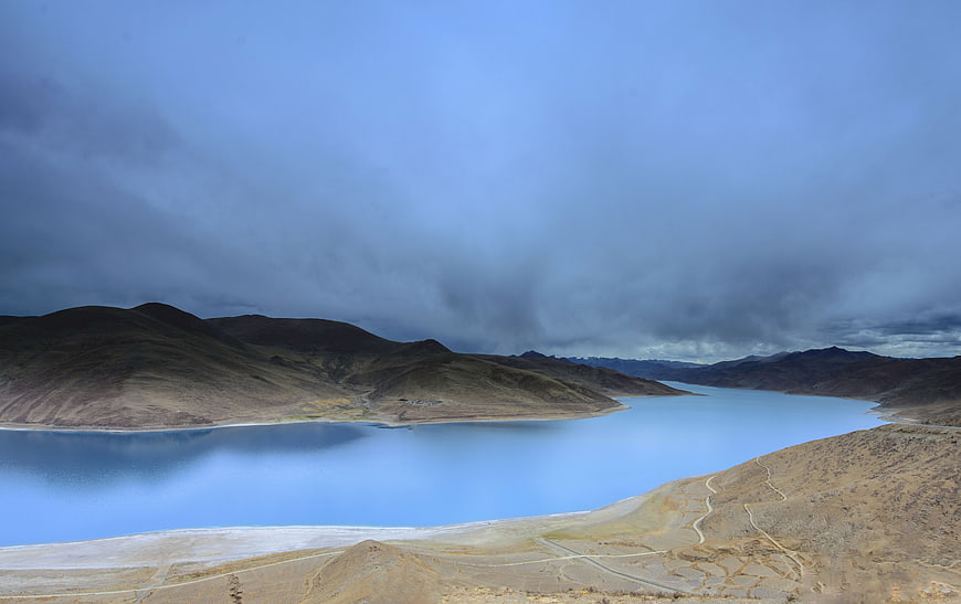 Dramatic landscape of a blue lake surrounded by hills under storm clouds